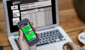 Person hält ein Smartphone mit einer Trading-App in der Hand, während auf dem Laptop eine gettex-Webseite mit Finanzdaten und Anlagezertifikaten geöffnet ist